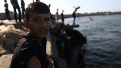 A boy sits by the water as children play, creating a lively scene in Gaza's coastal area.