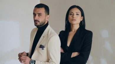 A man and woman posing confidently in stylish formal wear against a textured wall.